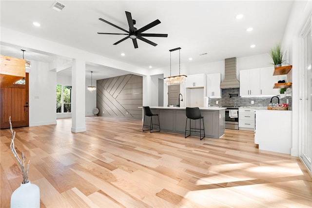 kitchen featuring white cabinetry, stainless steel electric range oven, hanging light fixtures, an island with sink, and custom range hood