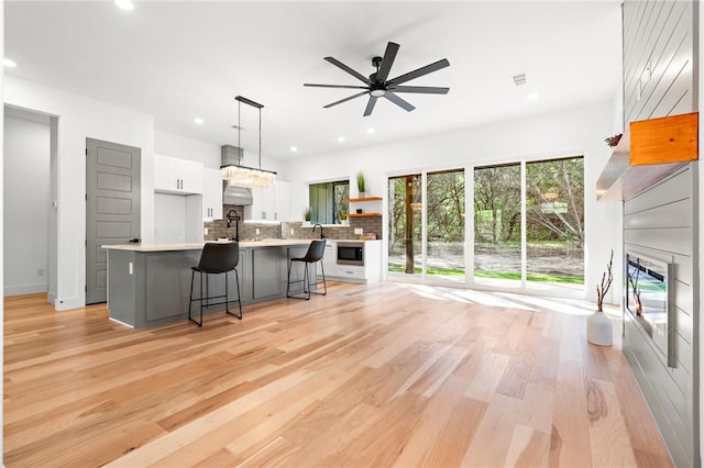 kitchen featuring white cabinets, decorative light fixtures, a kitchen bar, and light wood-type flooring