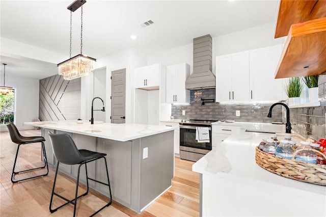 kitchen with stainless steel range with electric stovetop, custom exhaust hood, a center island, and decorative light fixtures