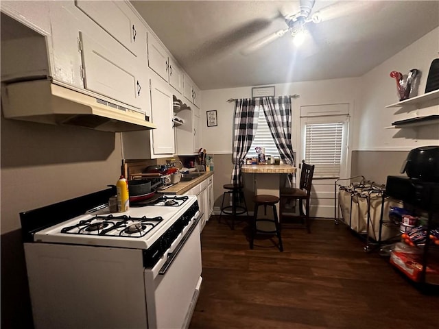 kitchen with white gas range, ceiling fan, dark hardwood / wood-style flooring, and white cabinets