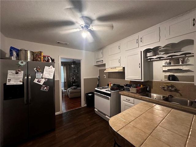 kitchen featuring stainless steel refrigerator with ice dispenser, white gas range, white cabinets, dark hardwood / wood-style floors, and tile counters