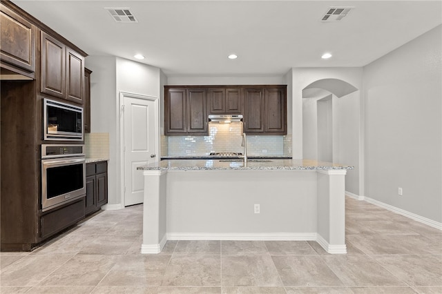 kitchen with dark brown cabinets, stainless steel appliances, and light stone counters