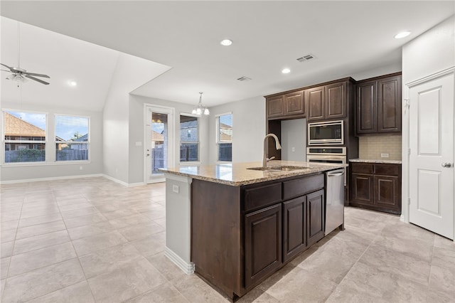 kitchen with backsplash, a kitchen island with sink, sink, appliances with stainless steel finishes, and dark brown cabinetry