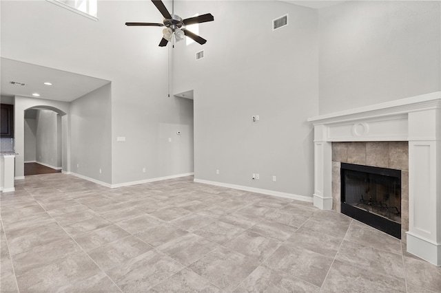 unfurnished living room with a tile fireplace, ceiling fan, and a high ceiling