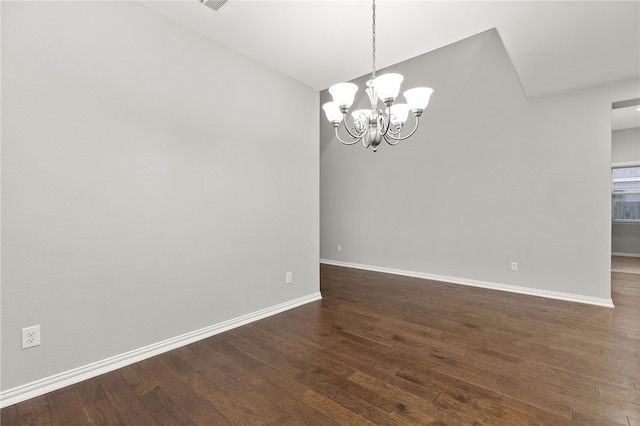 spare room featuring a chandelier and dark wood-type flooring