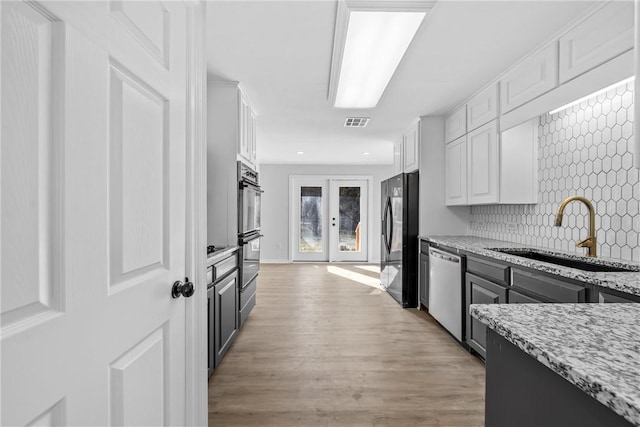 kitchen featuring black refrigerator, light stone countertops, sink, dishwasher, and white cabinetry