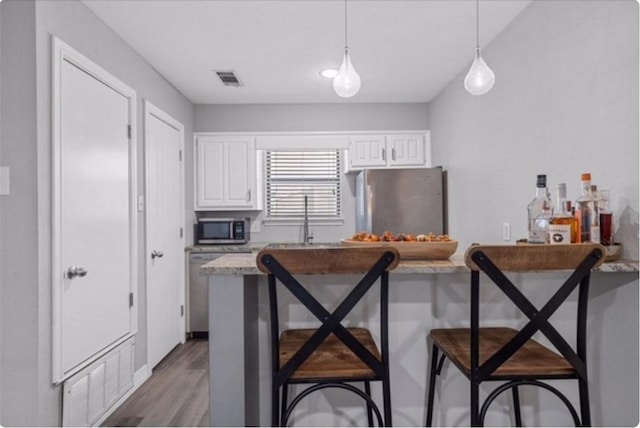 kitchen featuring a kitchen bar, white cabinetry, hanging light fixtures, and appliances with stainless steel finishes