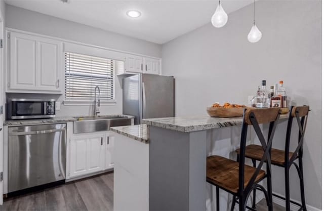 kitchen featuring white cabinetry, hanging light fixtures, dark hardwood / wood-style floors, a breakfast bar, and appliances with stainless steel finishes