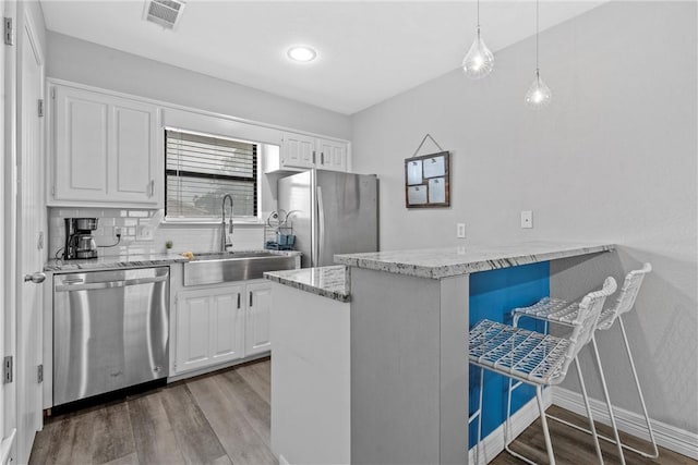 kitchen with sink, hanging light fixtures, stainless steel appliances, kitchen peninsula, and white cabinets