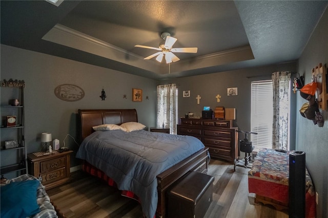 bedroom featuring ceiling fan, multiple windows, hardwood / wood-style floors, and a raised ceiling