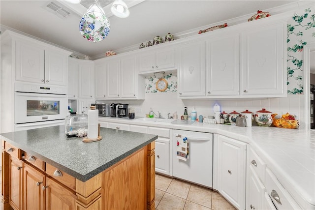 kitchen with ornamental molding, white appliances, sink, white cabinets, and a center island