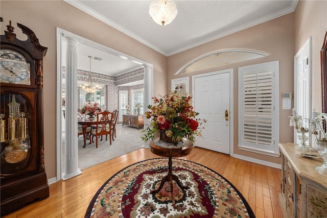 foyer entrance featuring light wood-type flooring, ornate columns, ornamental molding, a textured ceiling, and a notable chandelier