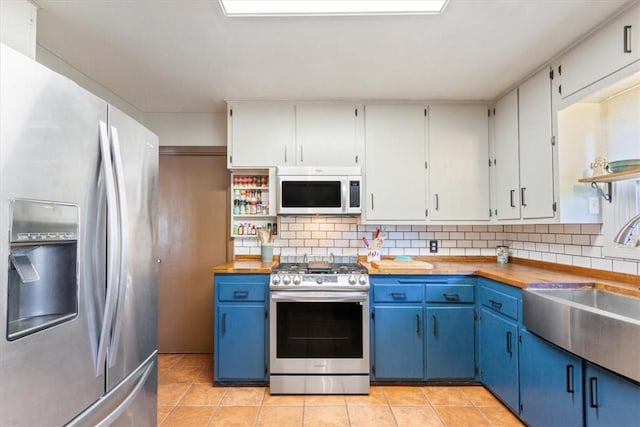 kitchen with light tile patterned flooring, blue cabinets, stainless steel appliances, and wood counters