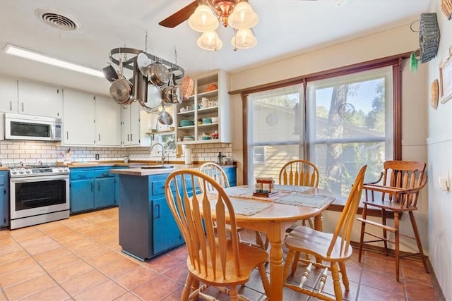 kitchen with white cabinets, light tile patterned flooring, blue cabinetry, and appliances with stainless steel finishes