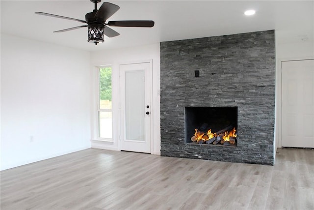 unfurnished living room featuring light hardwood / wood-style floors, a stone fireplace, and ceiling fan