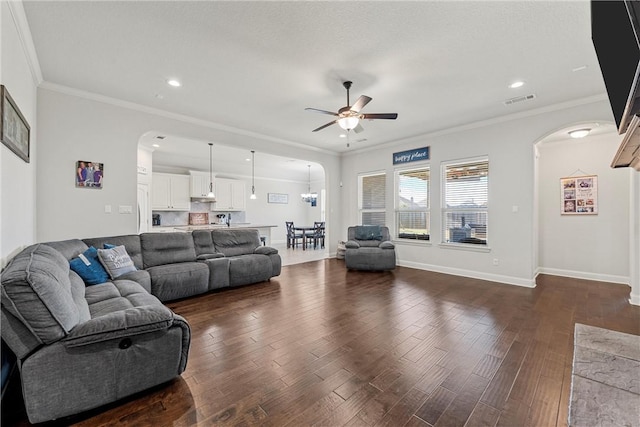 living room featuring ceiling fan with notable chandelier, ornamental molding, and dark wood-type flooring