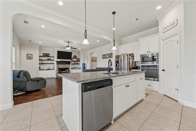 kitchen with appliances with stainless steel finishes, light tile patterned floors, white cabinetry, and a kitchen island with sink