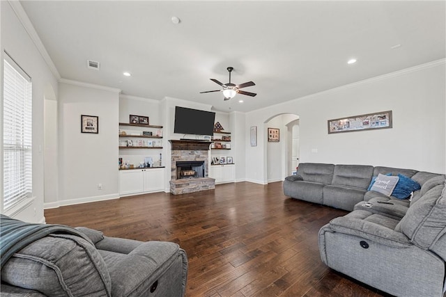 living room with ceiling fan, dark hardwood / wood-style flooring, a stone fireplace, and crown molding