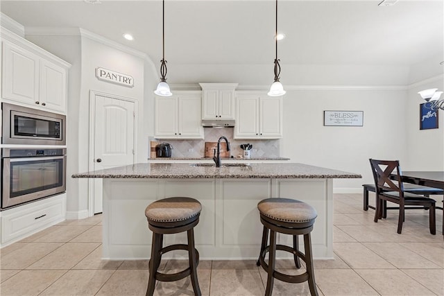 kitchen featuring a center island with sink, hanging light fixtures, sink, light stone counters, and appliances with stainless steel finishes