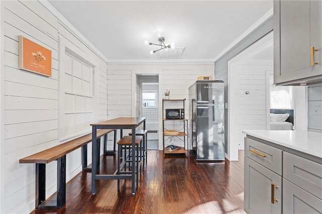 kitchen featuring gray cabinetry, wood walls, dark wood-type flooring, crown molding, and stainless steel fridge