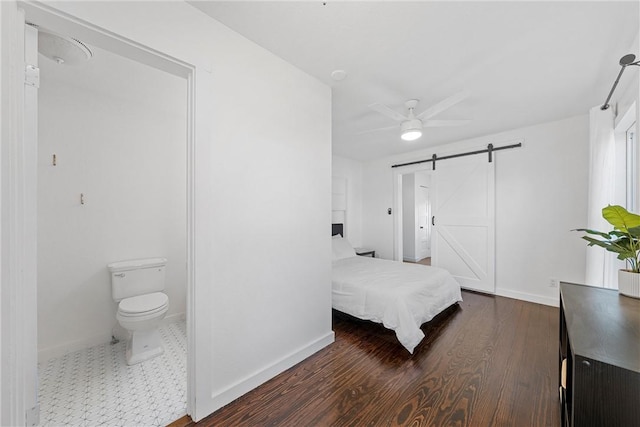 bedroom featuring a barn door, ceiling fan, dark wood-type flooring, and ensuite bathroom