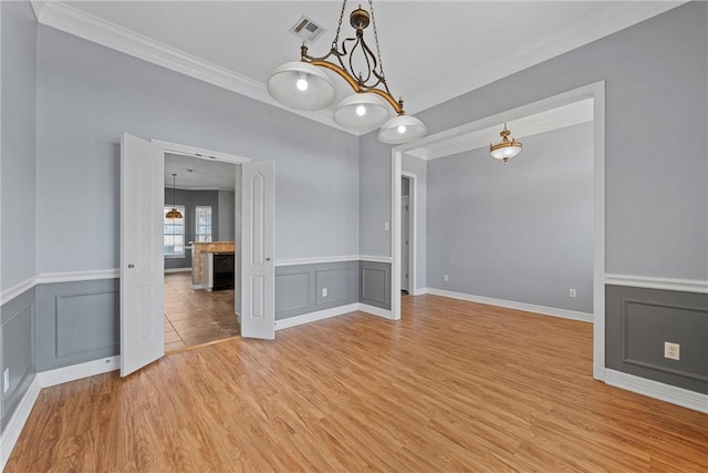 unfurnished room featuring visible vents, light wood-style flooring, crown molding, a fireplace, and a decorative wall