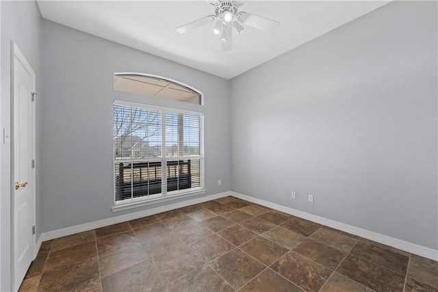 empty room featuring stone finish flooring, a ceiling fan, and baseboards