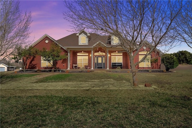 cape cod-style house with a porch, brick siding, and a yard