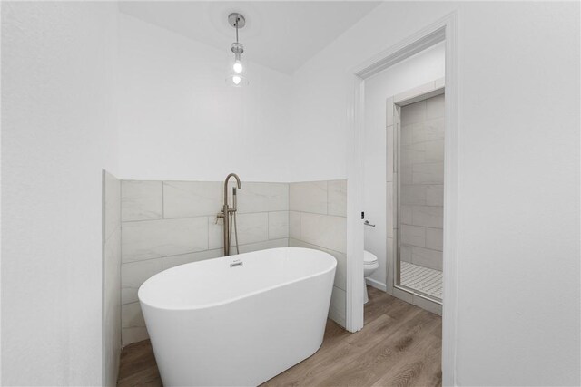 bathroom with hardwood / wood-style flooring, toilet, tile walls, and a tub