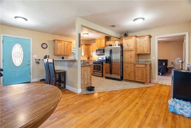 kitchen featuring a breakfast bar area, kitchen peninsula, light hardwood / wood-style floors, and appliances with stainless steel finishes