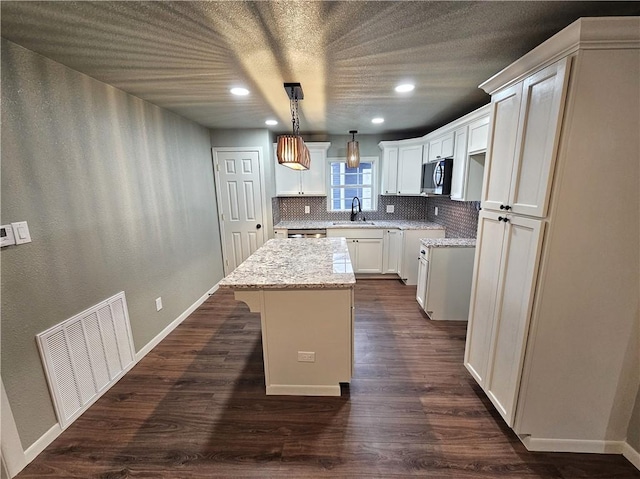 kitchen with pendant lighting, a center island, decorative backsplash, white cabinetry, and light stone countertops