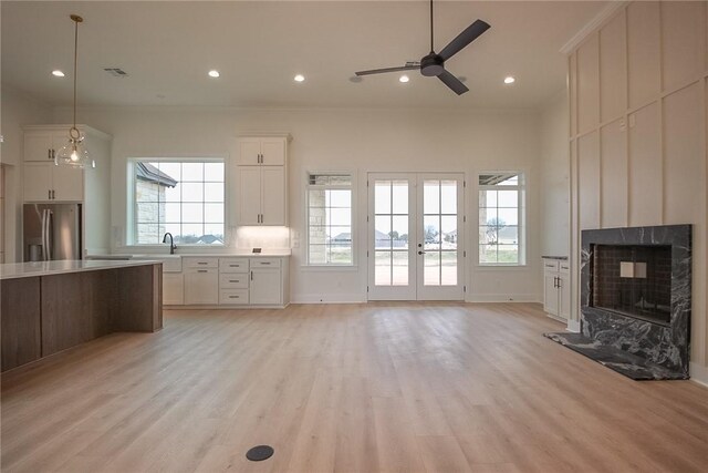 unfurnished living room with a high end fireplace, french doors, ceiling fan, light hardwood / wood-style flooring, and crown molding