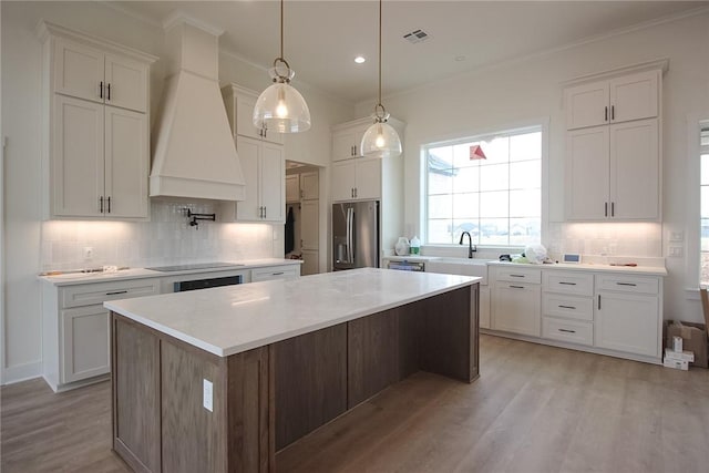 kitchen with appliances with stainless steel finishes, a center island, white cabinetry, premium range hood, and light hardwood / wood-style flooring