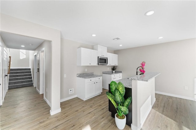 kitchen featuring light wood finished floors, stainless steel microwave, light stone counters, and visible vents