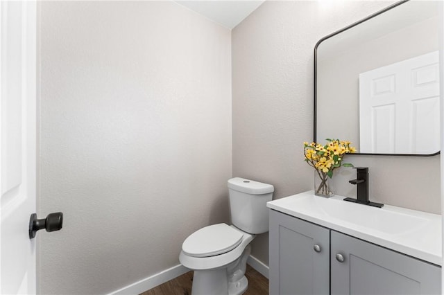 bathroom with baseboards, toilet, wood finished floors, and vanity