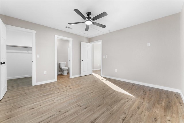 unfurnished bedroom with visible vents, a walk in closet, baseboards, light wood-style floors, and a closet