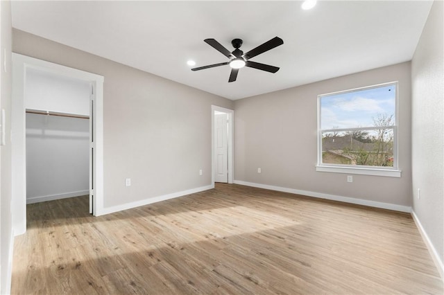 unfurnished bedroom with ceiling fan, baseboards, wood finished floors, and a spacious closet