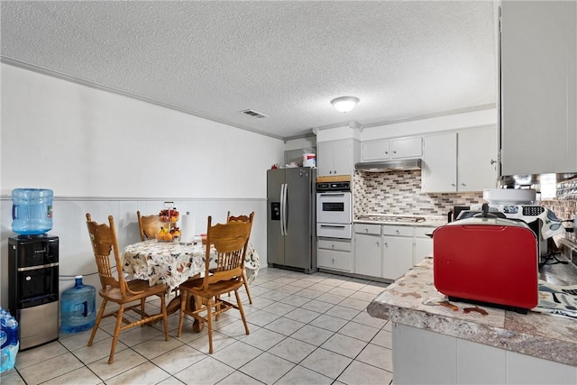 kitchen featuring light tile patterned floors, a textured ceiling, stainless steel appliances, and white cabinetry