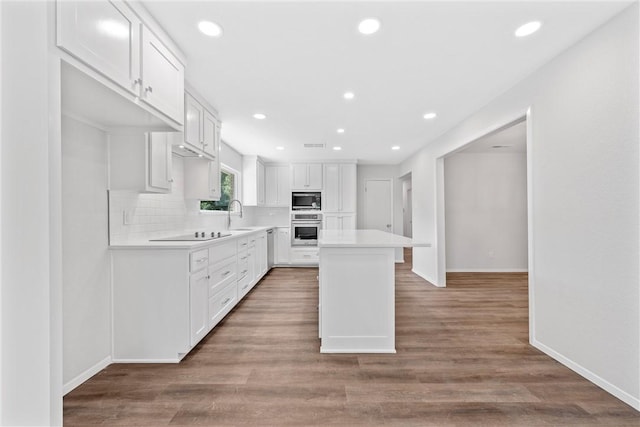 kitchen featuring appliances with stainless steel finishes, sink, hardwood / wood-style flooring, white cabinets, and a kitchen island