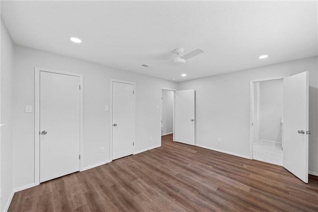 unfurnished bedroom featuring two closets, dark hardwood / wood-style floors, and ceiling fan