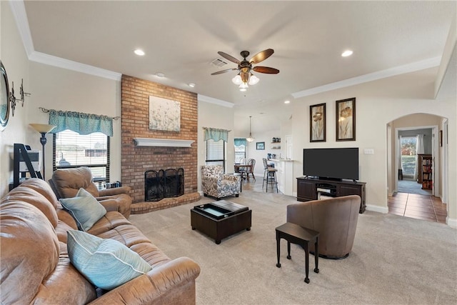 living room featuring ceiling fan, crown molding, light carpet, and a brick fireplace