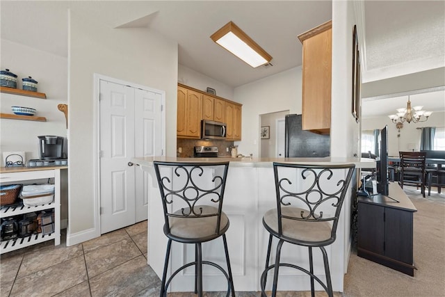 kitchen featuring kitchen peninsula, appliances with stainless steel finishes, a chandelier, and a breakfast bar area