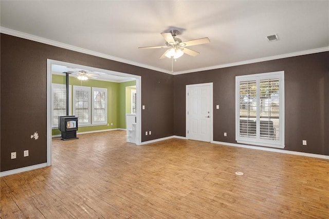 spare room featuring a wood stove, crown molding, light hardwood / wood-style flooring, and ceiling fan