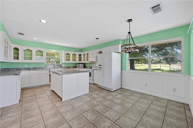 kitchen featuring light stone countertops, white cabinetry, hanging light fixtures, white appliances, and a kitchen island