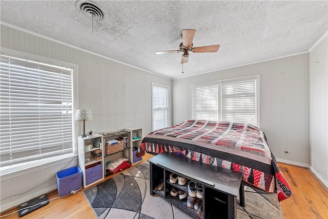 bedroom with ceiling fan, wood-type flooring, a textured ceiling, and ornamental molding