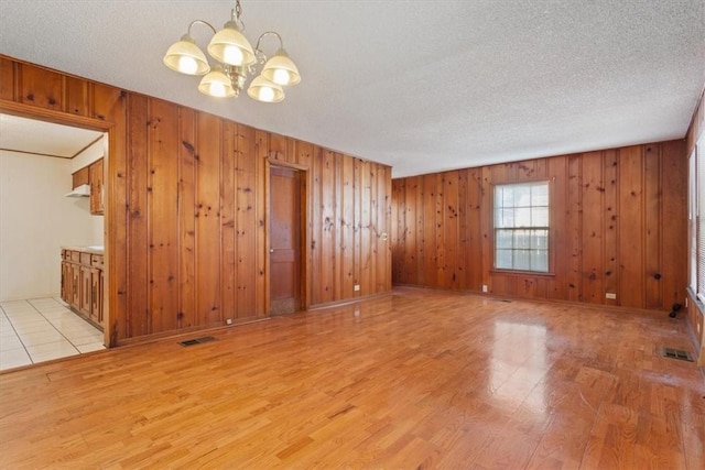 unfurnished room with a chandelier, a textured ceiling, wooden walls, and light hardwood / wood-style flooring