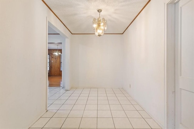 tiled empty room featuring a chandelier, a textured ceiling, and ornamental molding