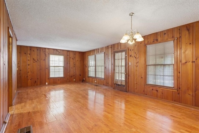 spare room with a textured ceiling, wooden walls, a notable chandelier, and light wood-type flooring