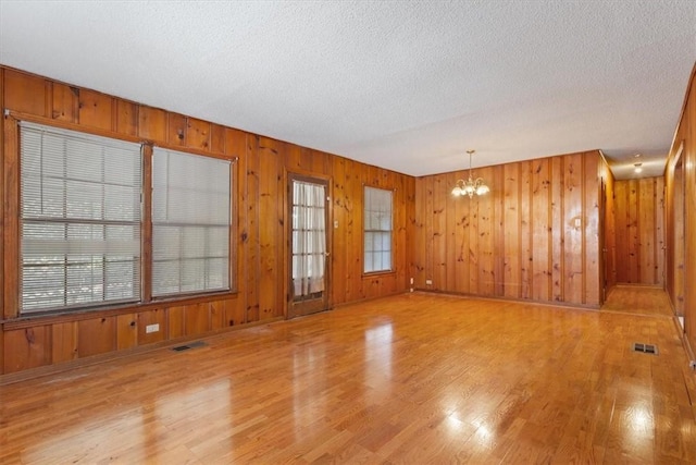 unfurnished room with light hardwood / wood-style floors, an inviting chandelier, a wealth of natural light, and wood walls