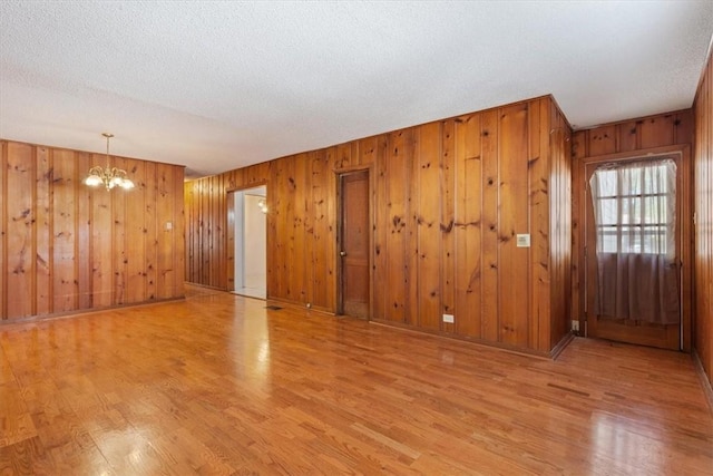 spare room with wood walls, light wood-type flooring, a textured ceiling, and a notable chandelier